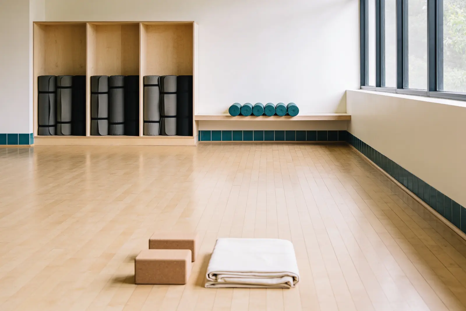 An empty fitness and yoga studio floor with rolled mats in an open shelving unit and cork blocks set out ready.