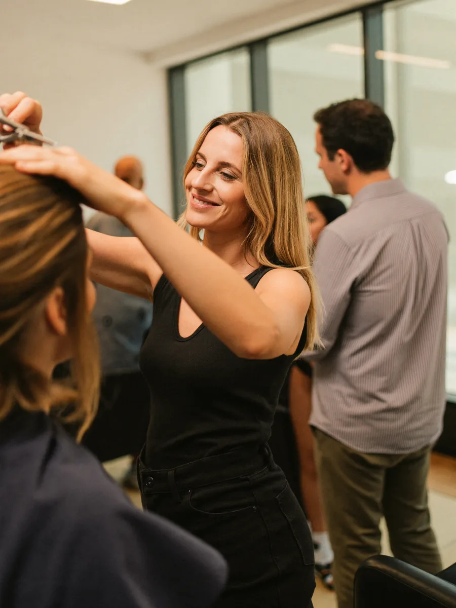 A salon owner in her styling chair area, scissors in hand, smiling between clients in a bright modern salon