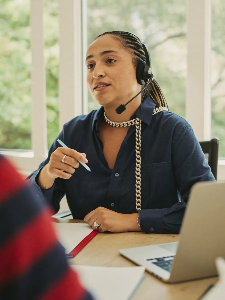 A language teacher in a one-to-one online lesson, headset on, notes beside the laptop