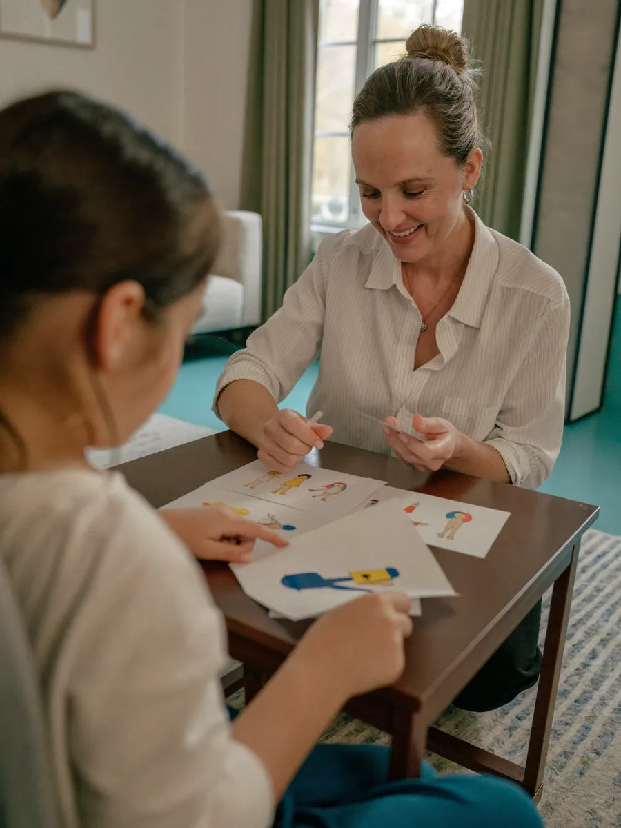 A speech therapist at a low table working through picture flashcards with a young child